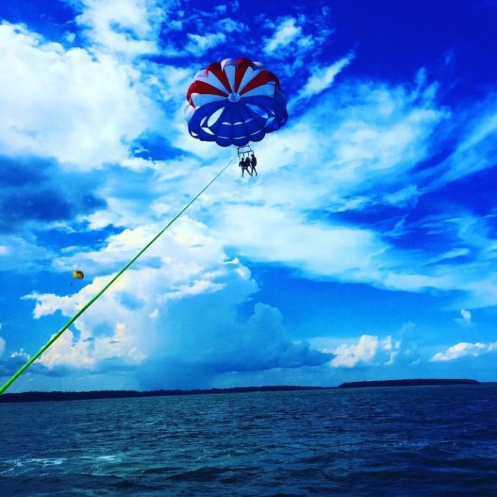 A red, white, and blue parasail in a cloudy blue sky