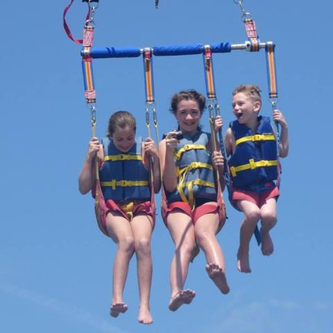 Three kids smiling as they hang in the sky from a parasail