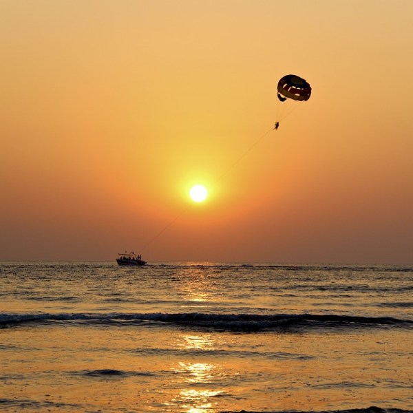 A boat and parasail silhouette in front of an orange sunset