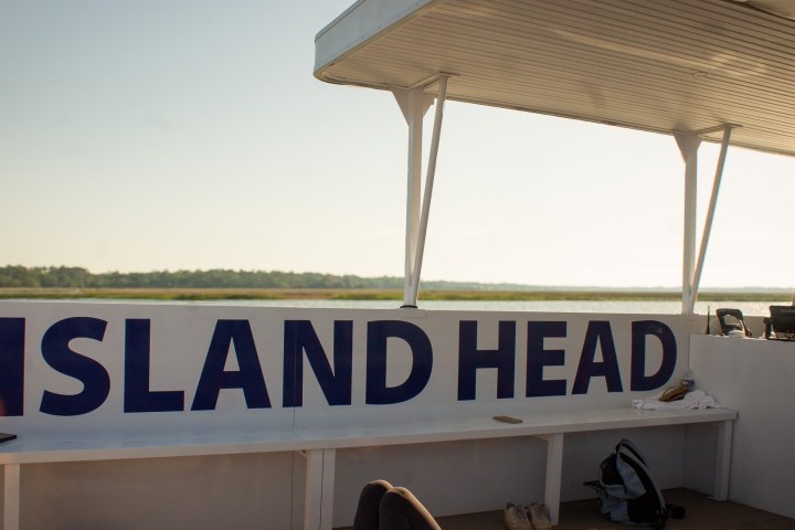 Person steering a boat with 'Island Head' sign on deck.