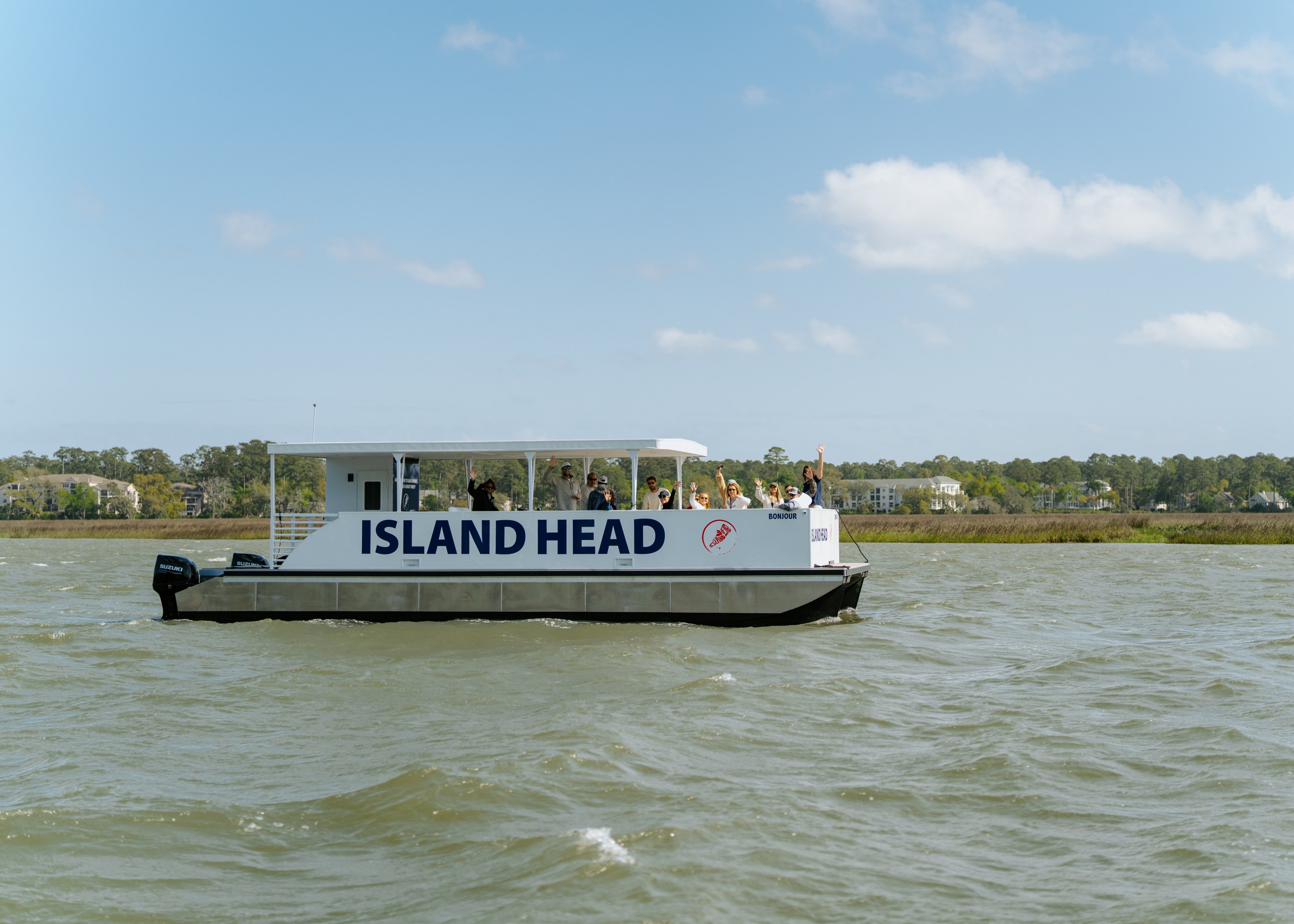 Boat named Island Head with people onboard cruising on a lake under a clear blue sky.