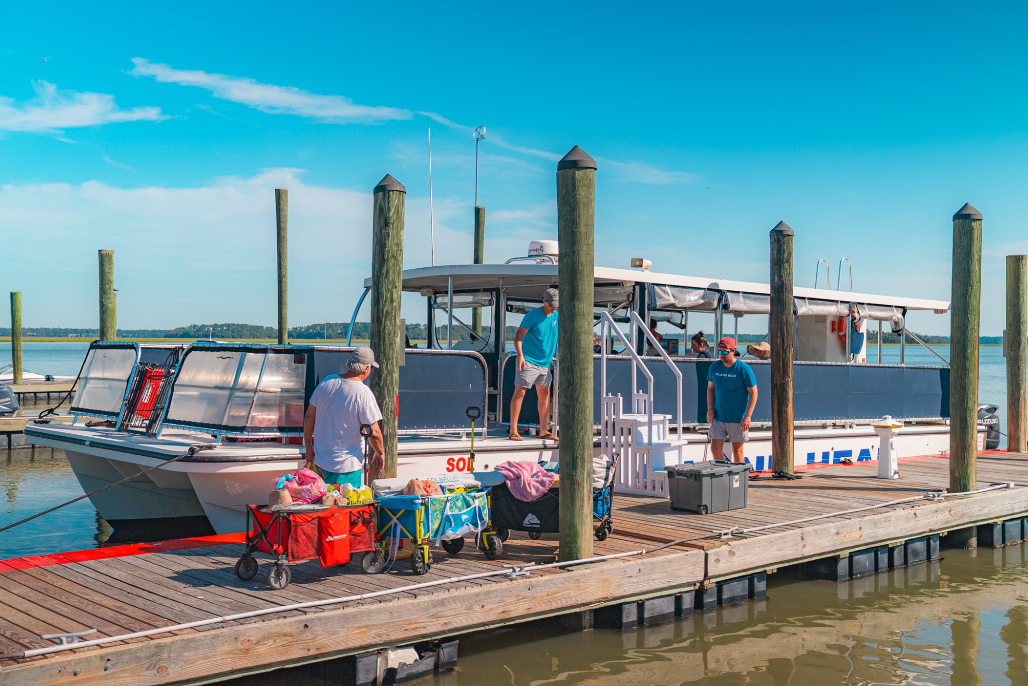 People loading supplies onto a tour boat docked at a wooden pier on a sunny day.