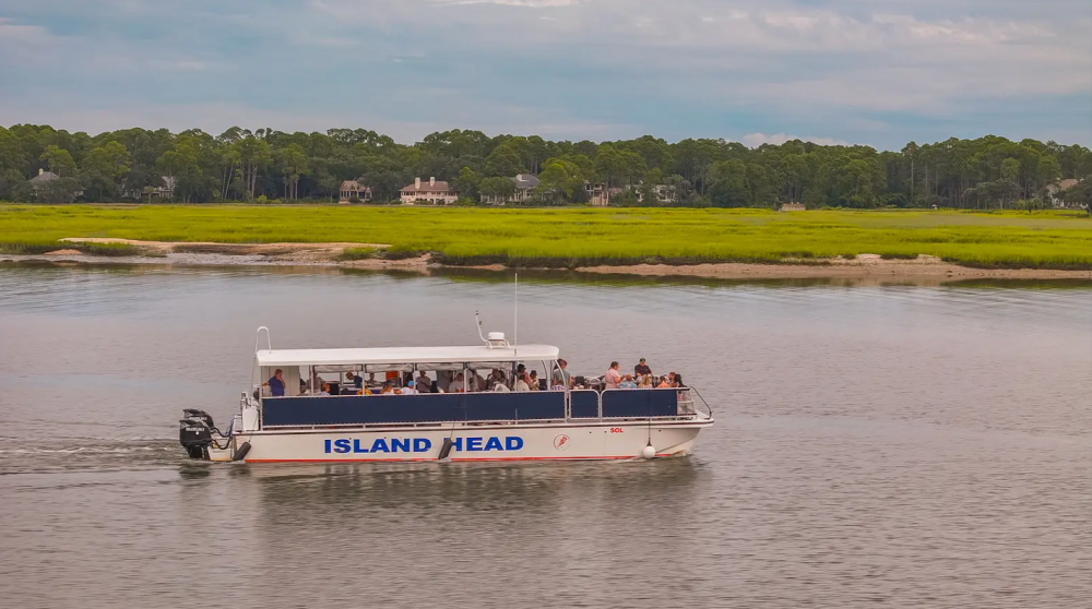 A blue and white tour boat named Island Head on a river with green shoreline.