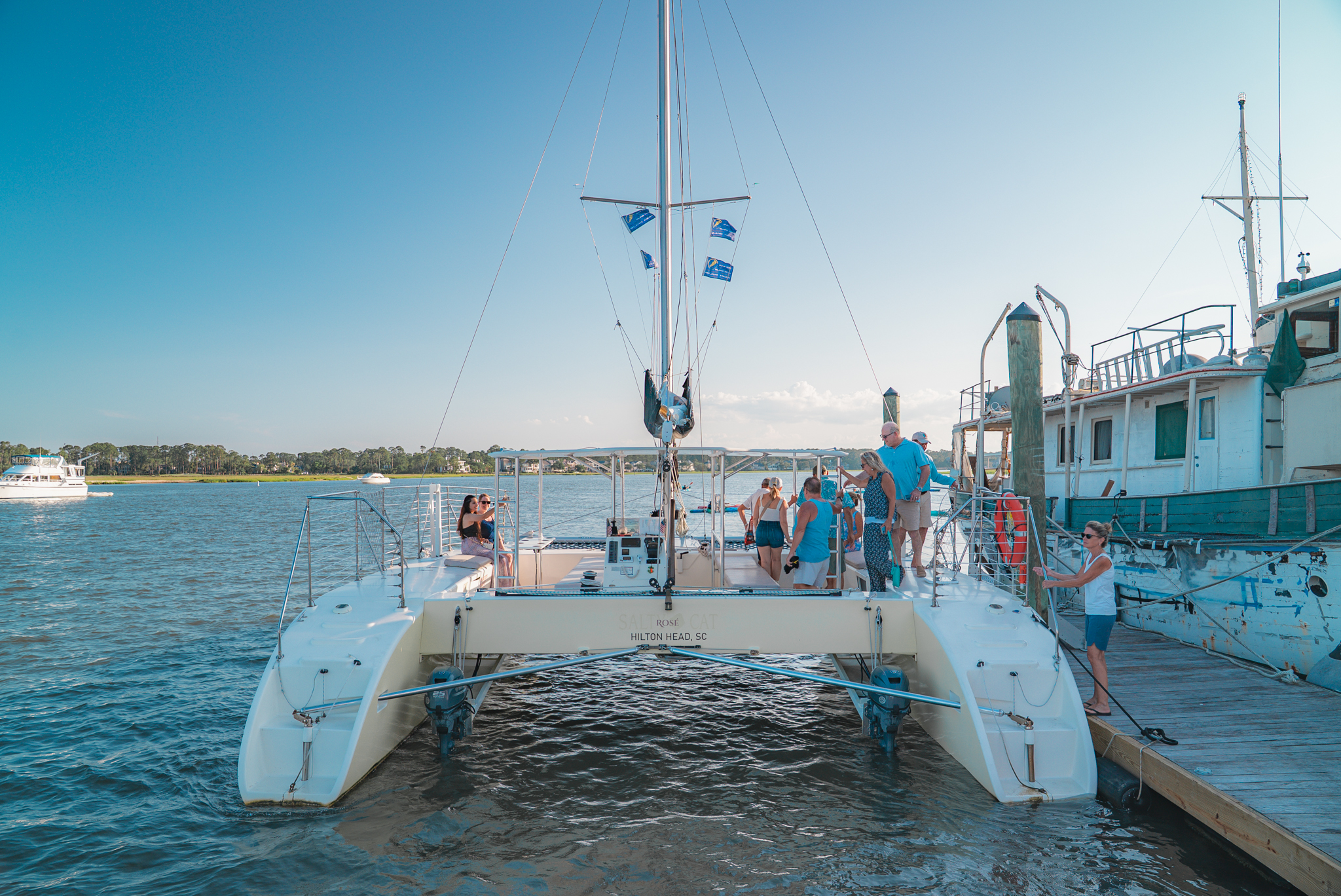 People boarding a catamaran docked by a pier on a sunny day.