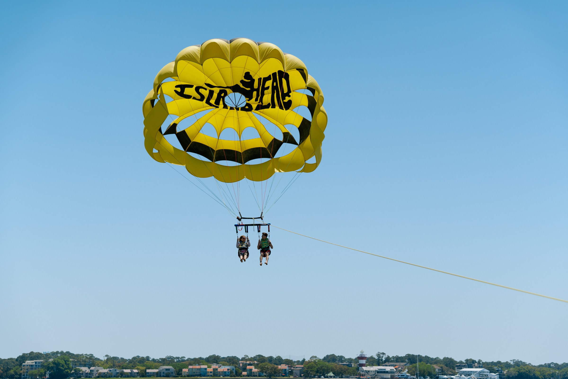 Two people parasailing with a yellow parachute against a clear blue sky.