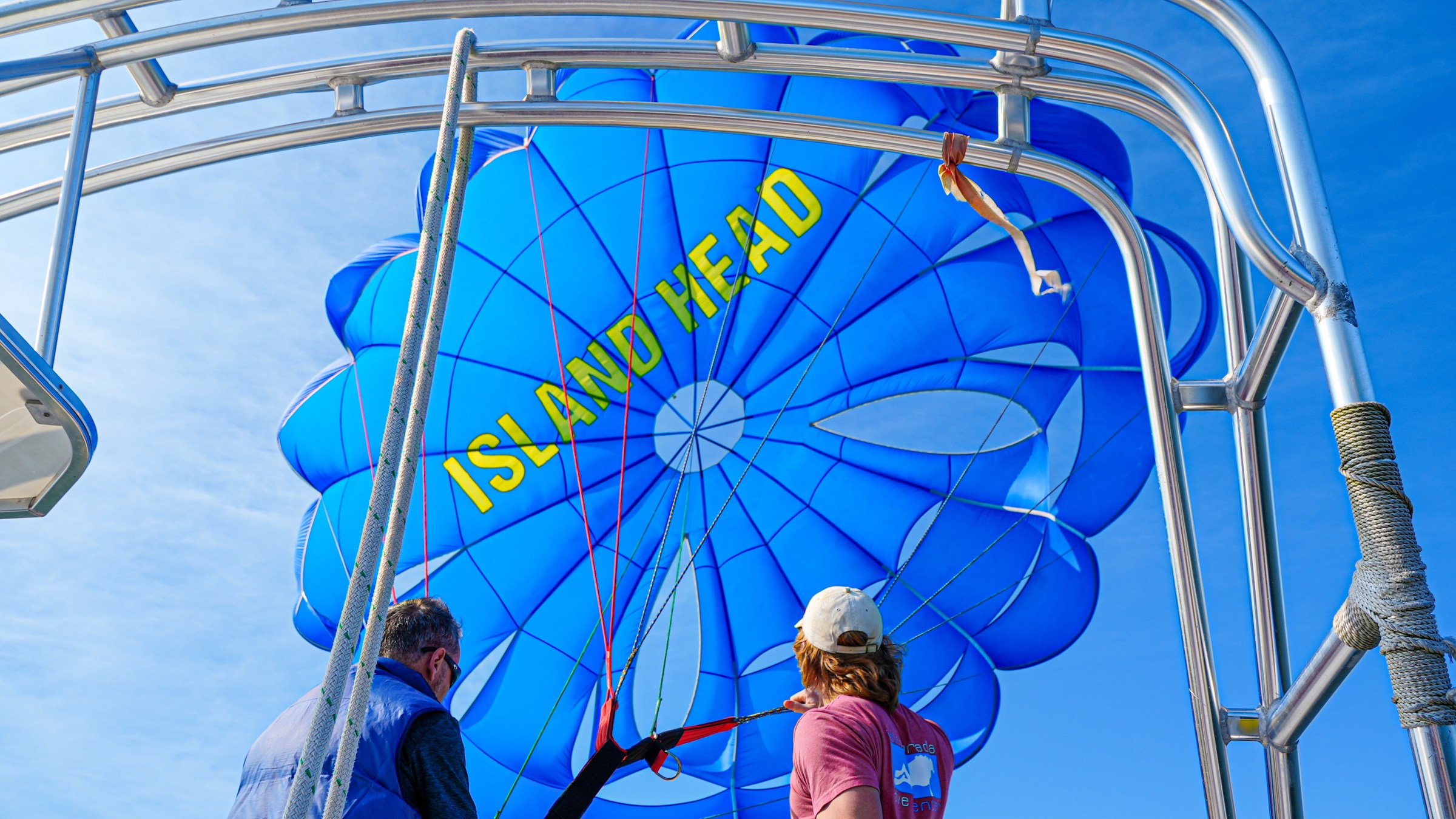 Two people on a boat setting up a blue parachute labeled 'Island Head'.